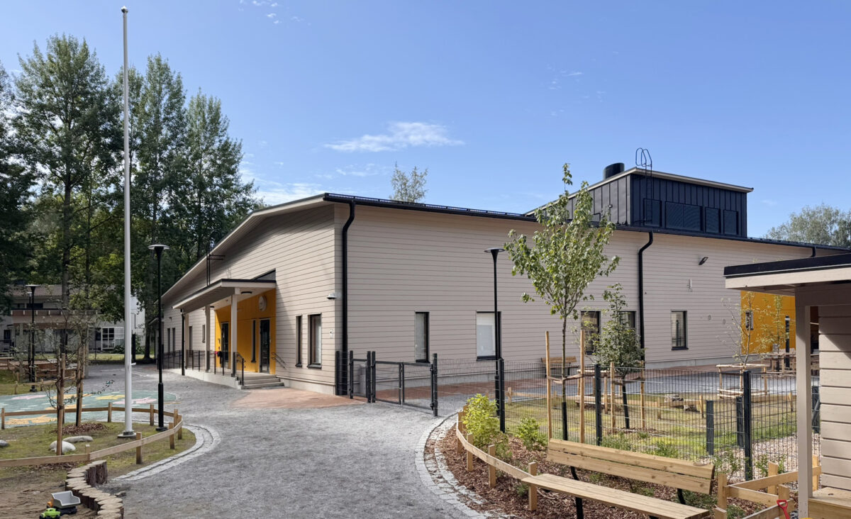 Päiväkodin leikkipiha, joka toteutettu mikrobiystävällisenä. Hirsirakennus, jossa on vaalea julkisivu.